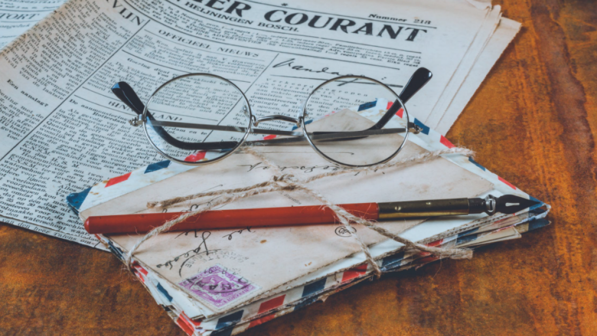round-framed glasses sitting on a pile of old letters with a newspaper in the background