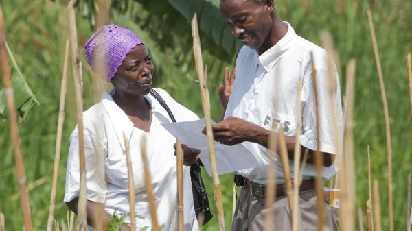 A man and a woman discussing a paper in the hands of the man in a rural area